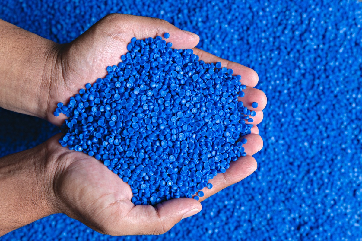 Hands holding a pile of blue plastic pellets against a background of scattered blue granules.