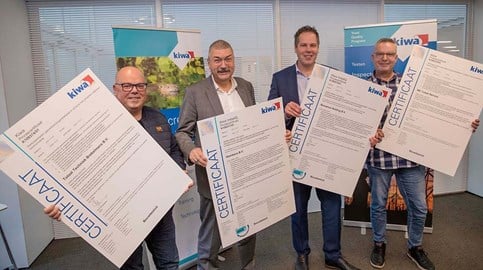 Four Kiwa clients stand in an office holding large certificates awarded by Kiwa, smiling as they celebrate the achievement