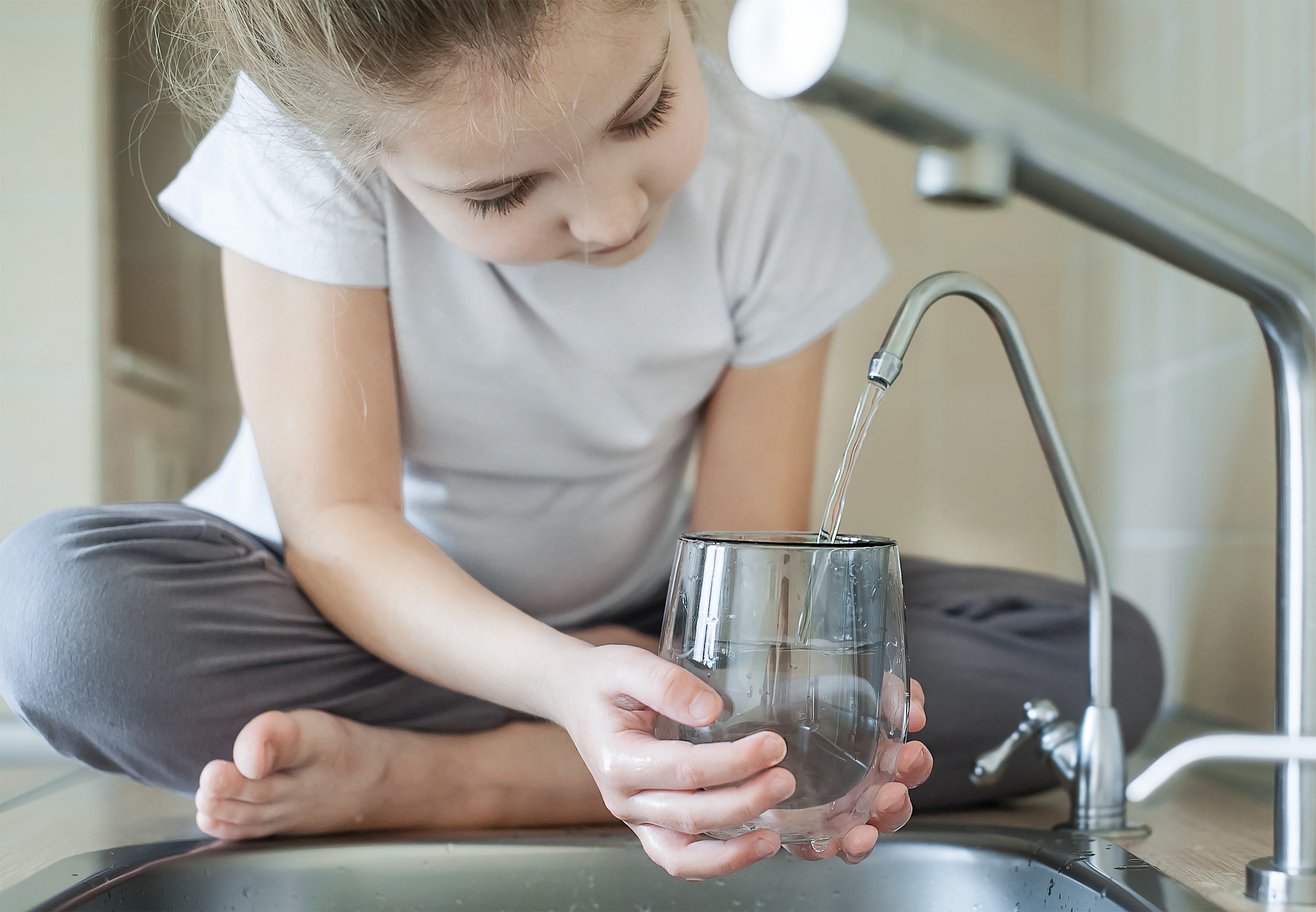 Young girl filling a glass with water from a kitchen faucet.